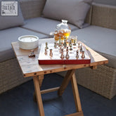 Red wooden chess set with metallic gold and silver pieces on a recycled teak wood square folding coffee table