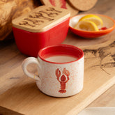 A white speckled ceramic mug with a hand painted red lobster design and red interior filled with milk