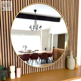 Round mirror with a thin matte gold metal frame mounted on wooden slat wall perfect for living rooms