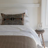 A rectangular pillow with bold black white and rust geometric circles on cotton percale resting on white fitted sheet