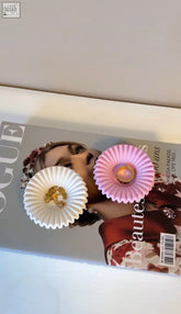A ripple trinket dish holding delicate white and pink cupcake liner earrings with sparkling gold chanel charms