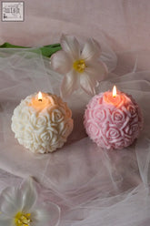 Two lit rose sphere candles in soft white and pink with intricate rose patterns casting a warm glow