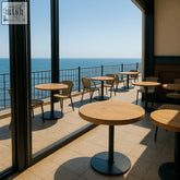 Round solid wood dining tables with black metal pole legs and matching chairs on a tiled balcony overlooking ocean