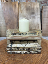 A cream candle sits on a weathered wooden indian pillar base candle holder with peeling paint for farmhouse decor