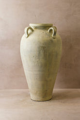 A tall off-white rustic indonesian pot made of ceramic with two looped handles perfect for decor or kitchen use