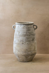 Rustic indonesian pot featuring a weathered off-white ceramic urn with loop handles and horizontal ridges
