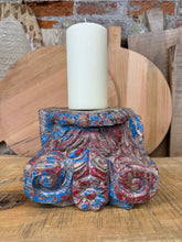 A white cylindrical candle on a weathered blue and red carved wooden indian pillar base candle holder for farmhouse decor