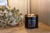 Black cylindrical sable 3 wick luxury candle with gold rim and label lit in a large candle collection
