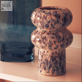 A small speckled vase made of ceramic with a brown and beige glaze and two rounded bulbous sections stacked vertically