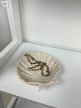 A textured off-white ceramic shell trinket dish holding a gold chain for seaside elegance and coastal charm