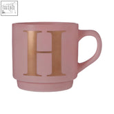 Matte pink ceramic monogram mug with a large metallic gold h and smooth rim for stylish sipping