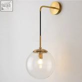 A sleek brass wall light with a clear glass globe and black accent rod from the sizzle mid-century hanging wall light collection