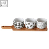 Set of three white ceramic patterned dishes with black geometric designs on a wooden soiree serving board
