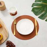 Sophistimat brown leather placemat with subtle stitched edge under white plate and gold utensils in dining setup