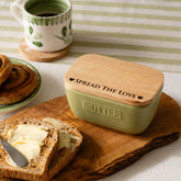 A sage green ceramic butter dish with a natural wood lid engraved spread the love with a matching knife set