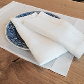White linen stanhope napkins with delicate hemstitching on a blue and white patterned plate for elegant dining
