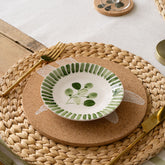 A hand painted white ceramic stripe flora side plate with green leafy design and striped rim on a cork coaster