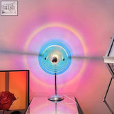 A sleek sunset table lamp with a translucent blue circular shade and metallic base casting vibrant rainbow light patterns