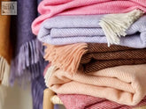 A stack of sweet shop herringbone wool throws in soft pastel hues with fringed edges made from pure new wool
