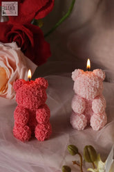 Two lit teddy rose-shaped candles in vibrant red and soft pink with detailed floral wax textures teddy bear style