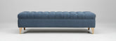 The barton foot stool is a blue tufted velvet storage bench with light wood legs perfect for extra seating or storage
