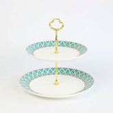 The edwardian bone china cake stand features a two-tiered white ceramic plate with teal geometric patterns and gold handles