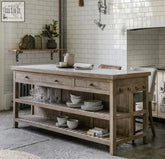 Rustic wooden manor kitchen island with light gray stone countertop, three drawers, and open shelving for storage