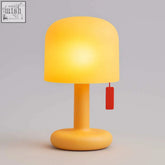A warm yellow mini ambient desk lamp with a matte finish and a small red pull cord for easy lighting