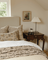 Beige floral quilted bedspread with leaf pattern draped over white bedding featuring the moon garden kantha throw