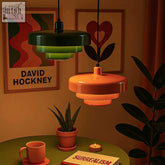 Two tiered retro pendant lights in dark green and warm orange with sleek metallic fixtures hanging from black cords