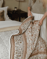 The reverse paisley quilt is a soft cream-colored quilt with intricate brown and gray floral embroidery along edges
