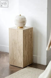 A white layered ceramic lamp with a gold base on a travite side table with a beige marble pedestal table