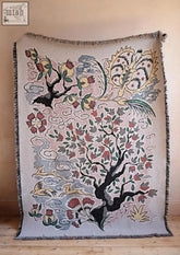 Beige woven tapestry tree of life blanket with vibrant pink and red blossoms black branches yellow birds and clouds