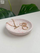 A pink speckled terrazzo trinket bowl holding gold-toned rings and chain necklace perfect as a thoughtful gift