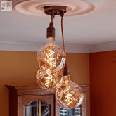 Three glowing clear glass organic neo bulbs with intricate coils hang from a dark metal triple cluster pendant light