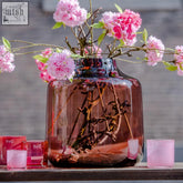 A mouth blown translucent rose colored glass vase from the dutz collection with a glossy finish and dutz logo