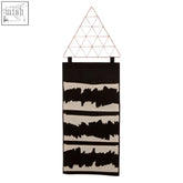 Black wall hanging pocket organiser with black and cream abstract tapestry and triangular wireframe top