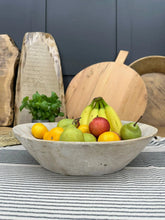A rustic light gray stone bowl with fresh fruits in a vintage bleached wooden serving bowl for antipasti and cheese