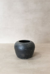 A vintage dark ceramic jar with a matte black finish, rounded tapered body, and subtle embossed patterns vintage dark pot n° 46