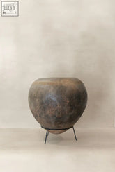 A vintage nupe pot with a weathered round ceramic body and rustic brown gray patina on a black metal stand