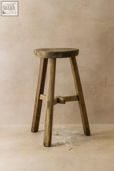 Vintage rustic elm wood stool with round weathered seat and three sturdy legs joined by crossbar