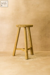 Vintage rustic elm wood stool with round light-colored seat and three sturdy legs connected by a crossbar