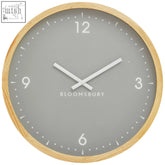 A vitus grey wall clock with a sleek grey face, natural wood frame, minimalist white numerals, and bloomsbury branding