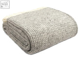 A neatly folded silver grey waffle xl pure new wool throw with a textured herringbone pattern and blanket size guide