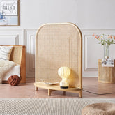 Beige woven waite rattan room divider with curved top wooden base and shelf holding a glowing lamp