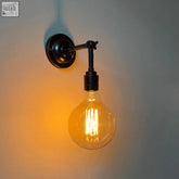 A warm glowing traditional wall light with black metal lamp holders and amber glass bulb showing filament wires