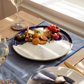A large rustic ceramic plate with a speckled white and deep blue hand painted glaze and irregular rim design
