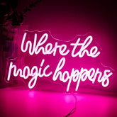 A glowing pink led neon sign with where the magic happens in white cursive for bedroom wedding birthday decor