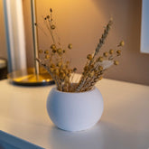 White concrete round pot with dried golden seed pods and wheat stalks in a handmade concrete planter style