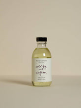 A clear glass bottle with black cap containing pale yellow wild fig and saffron diffuser refill with free reeds and vegetable oil base
